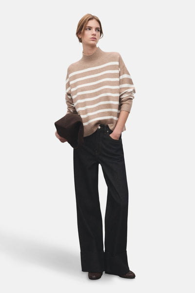Pull à col rond beige MANGO à rayures horizontales blanches, porté avec un jean large bleu foncé.