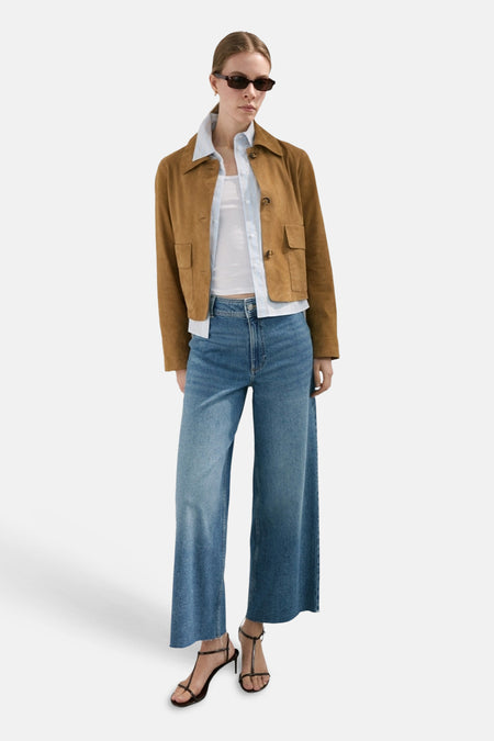 Jean large en denim bleu moyen de MANGO, porté avec une veste marron courte et des sandales à talons.