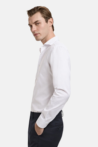 Wit overhemd met lange mouwen van MANGO, gedragen door een man met een marineblauwe broek, van opzij gezien.