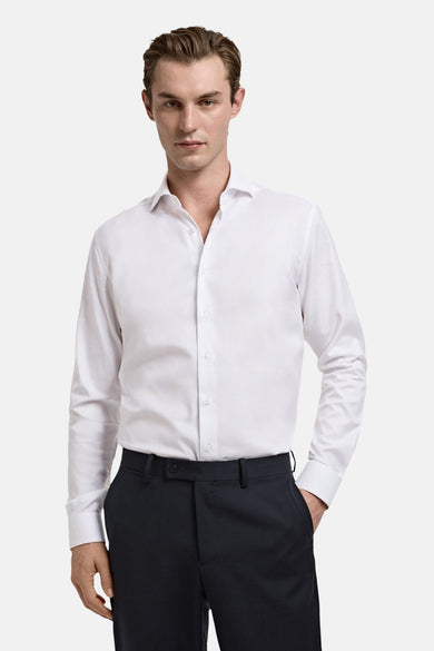 Wit overhemd met lange mouwen van MANGO, gedragen met een donkere pantalon, hand in de zak.