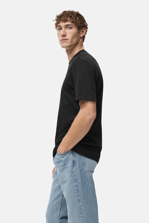 T-shirt à manches courtes noir de MANGO, porté par un homme en jeans bleu, vue de côté.