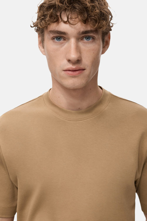 T-shirt à manches courtes beige de MANGO, porté par un homme aux cheveux bouclés et aux yeux bleus.
