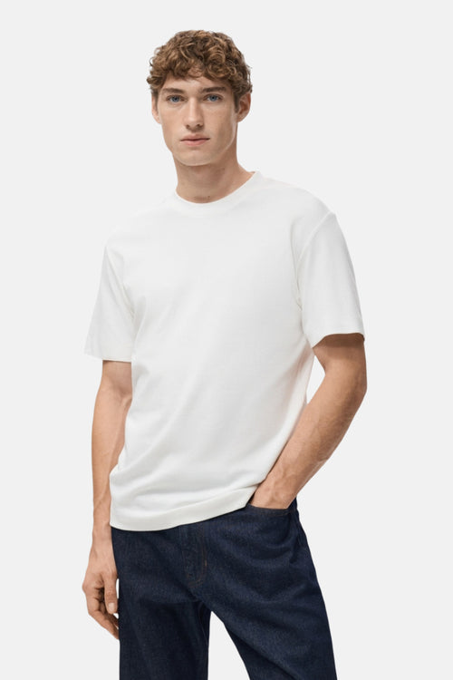 T-shirt blanc à manches courtes de MANGO, porté avec un jean foncé, main dans la poche.