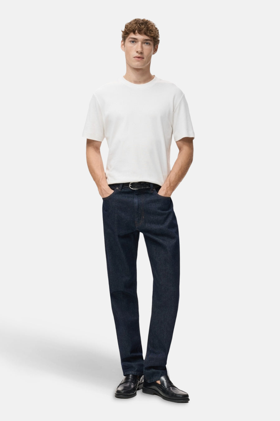 Witte t-shirt met korte mouwen van MANGO, gedragen met een donkere blauwe broek en zwarte mocassins.