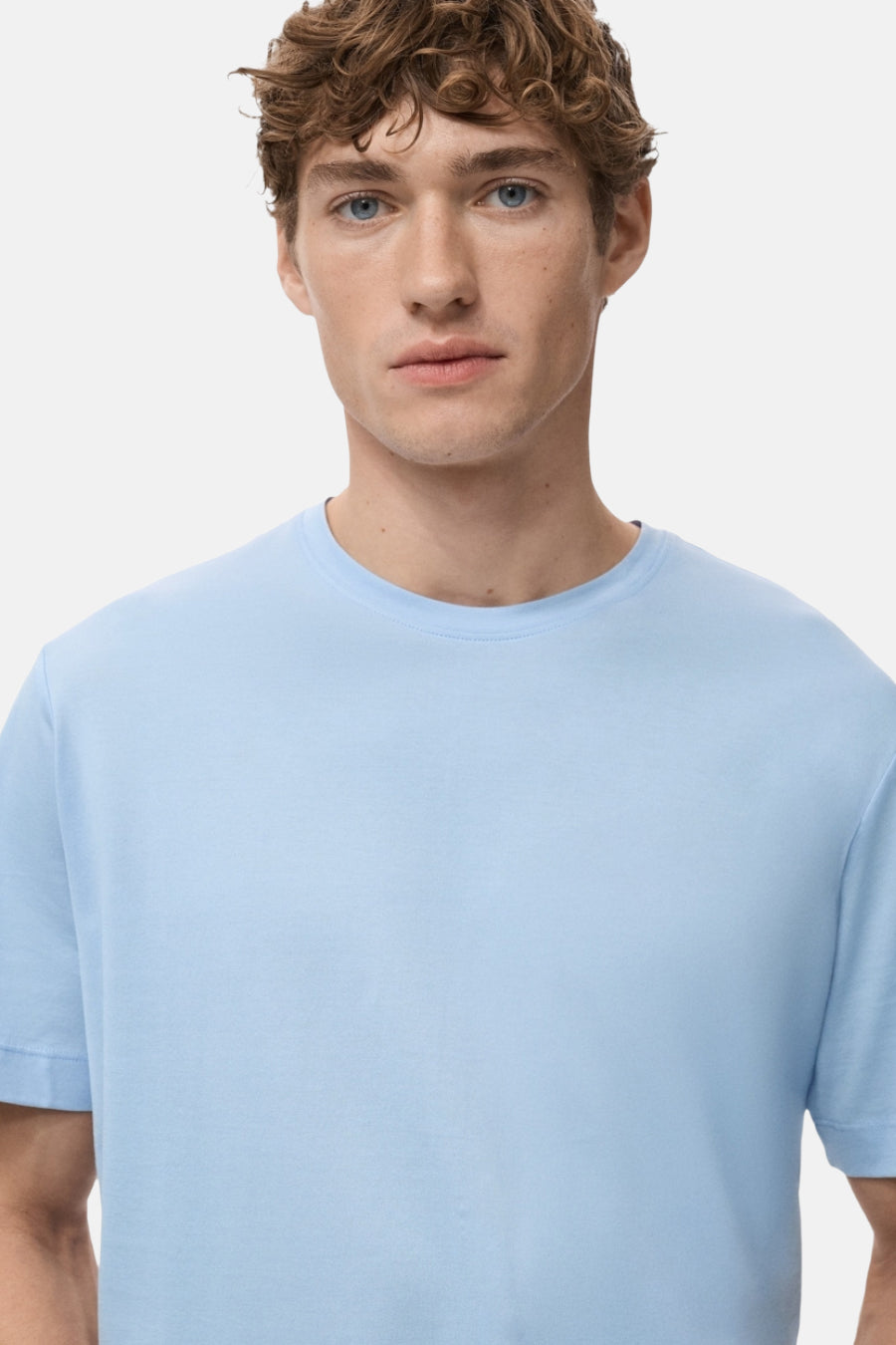T-shirt bleu à manches courtes de MANGO, porté par un homme aux cheveux bouclés.
