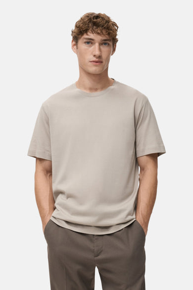 T-shirt beige à manches courtes de MANGO, porté avec un pantalon marron et un fond uni.