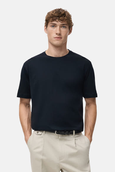 T-shirt à manches courtes bleu de MANGO, porté avec un pantalon clair et une ceinture noire.