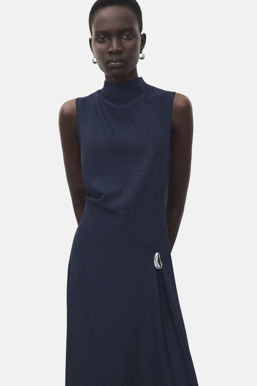 Blauwe jurk van MANGO, midi-lengte, met opstaande kraag en decoratief metalen detail aan de zijkant.