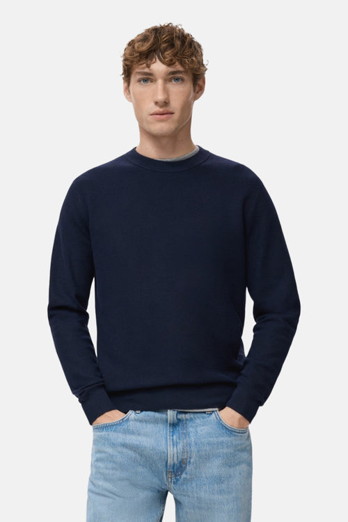Pull bleu à col rond de MANGO, porté sur un t-shirt gris avec un jean décontracté.
