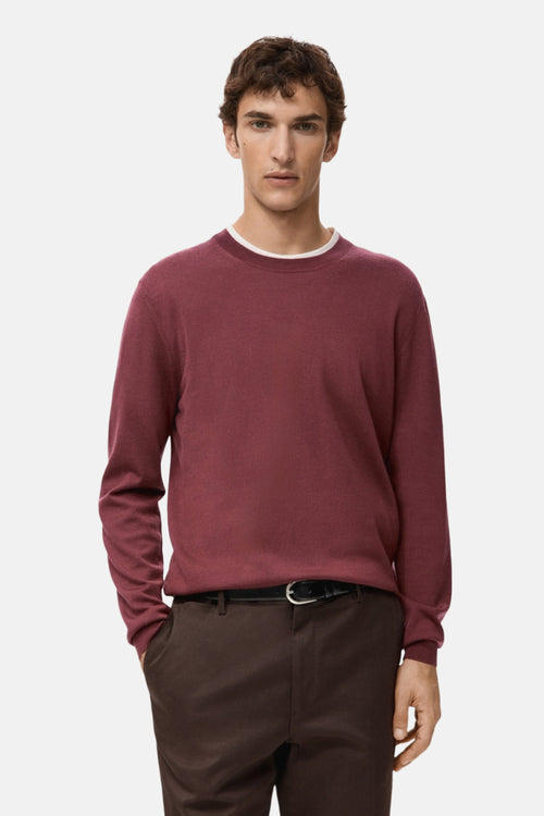 Pull à col rond rouge de MANGO, porté avec un pantalon marron et une ceinture noire.