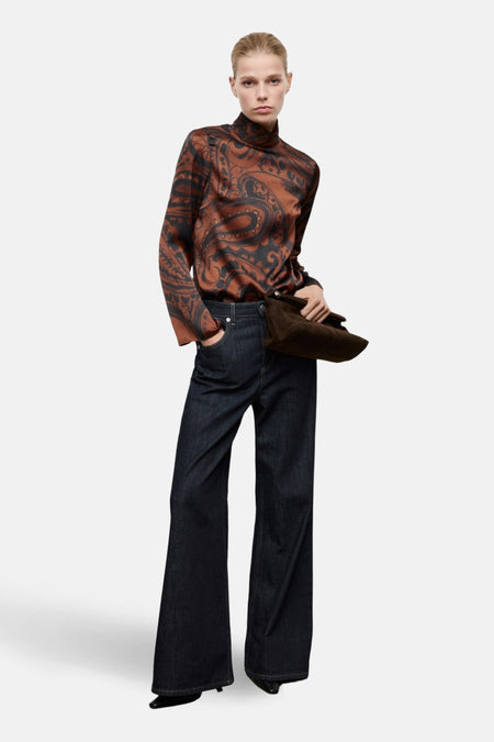 Chemisier à manches longues marron à motif cachemire de MANGO, porté avec un pantalon évasé en denim brut et un sac en daim marron.
