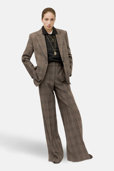 Bruine blazer van MANGO, geruit, gedragen met een grijze trui en gouden kettingen.