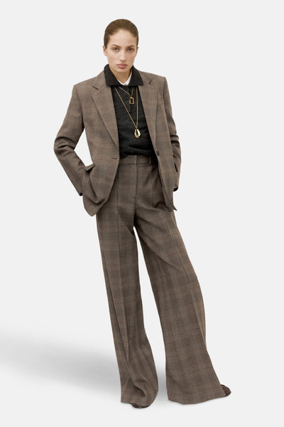 Bruine blazer van MANGO, geruit, gedragen met een grijze trui en gouden kettingen.