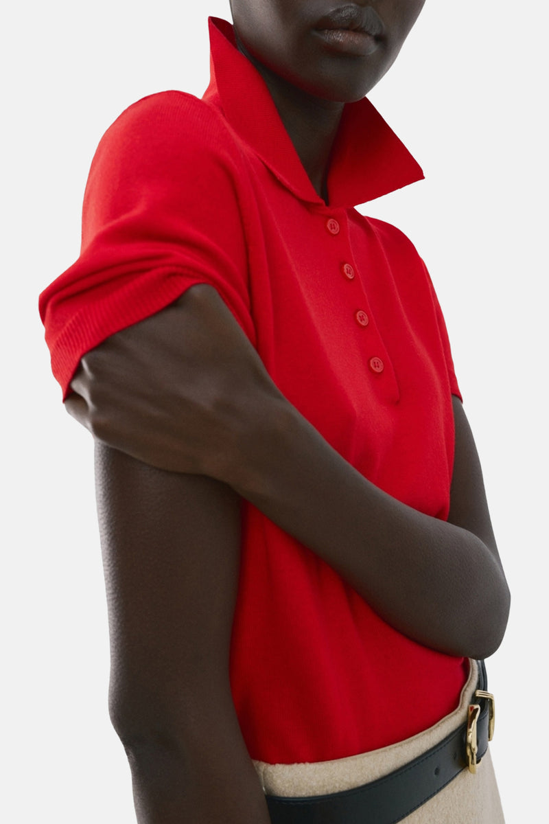 Rood poloshirt met korte mouwen van MANGO, gedragen met een beige uitlopende rok en een zwarte riem, van achteren gezien.
