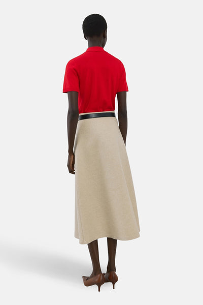 Polo à manches courtes rouge de MANGO, porté avec une jupe beige évasée et une ceinture noire, vue de dos.
