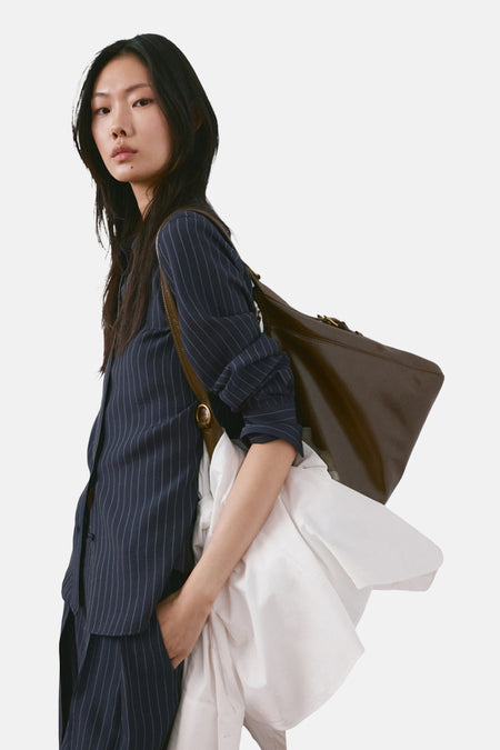 Chemise à manches longues bleue à rayures, de MANGO, portée avec un pantalon assorti et un sac marron.