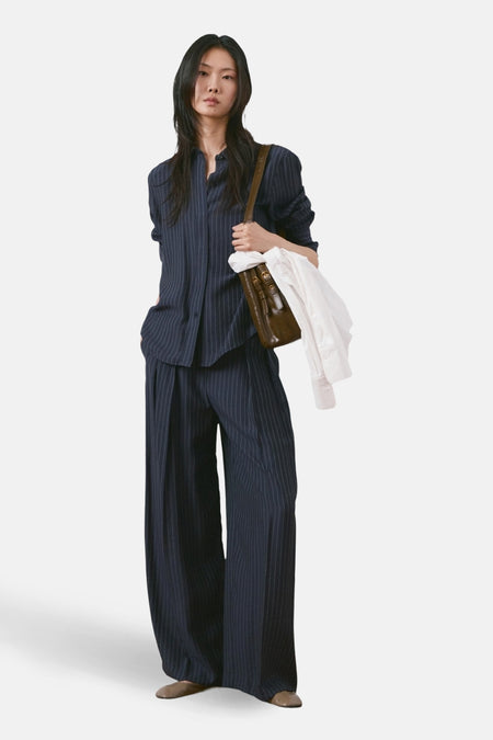 Chemise à manches longues bleue à rayures fines de MANGO, portée avec un pantalon assorti et un sac marron.