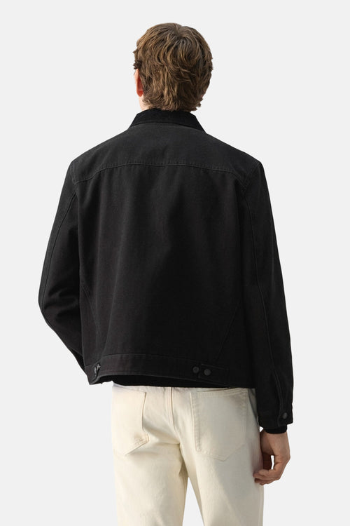 Veste courte noire de MANGO, vue de dos, portée avec un pantalon beige.