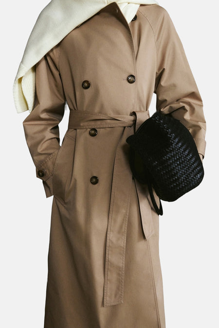 Veste longue beige de MANGO, avec ceinture nouée et poches, portée avec un pull blanc.
