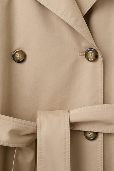 Veste longue beige de MANGO, avec une ceinture ton sur ton et des boutons marrons.
