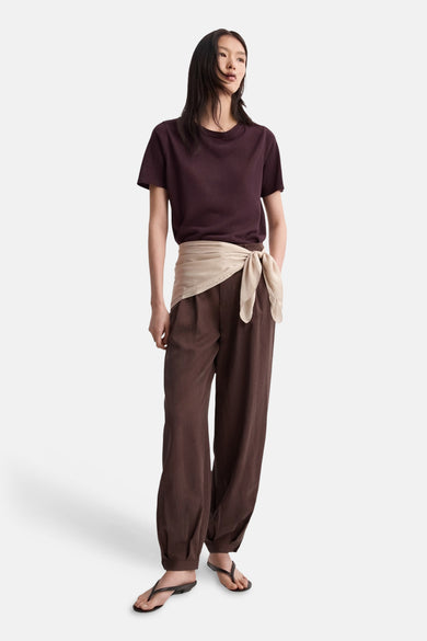 Bordeaux ronde hals trui van MANGO, gedragen met een bruine broek met strikceintuur en zwarte sandalen.