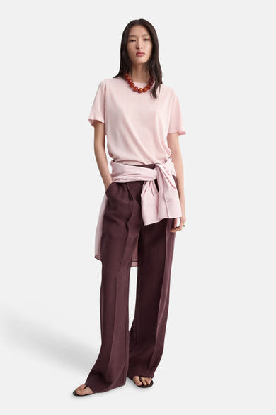 Roze trui met ronde hals van MANGO, gedragen met een bordeauxrode wijde broek en een parelketting.