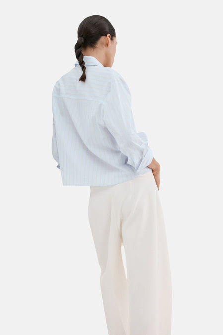 Chemise à manches longues bleue rayée de MANGO, portée avec un pantalon blanc et coiffure tressée, vue de dos.