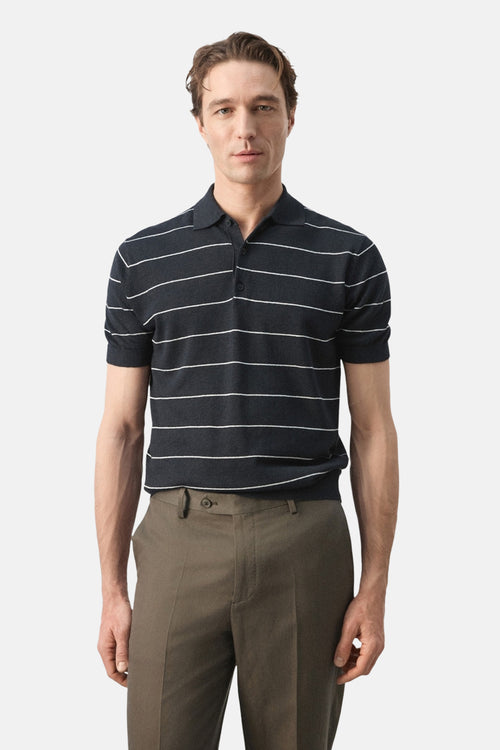 Polo noir à rayures blanches de MANGO, porté avec un pantalon marron et un bouton apparent.