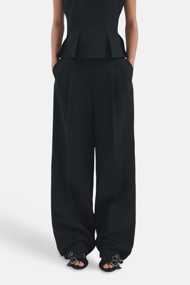 Pantalon bleu de MANGO, coupe large, avec des plis et porté avec des sandales à brides.
