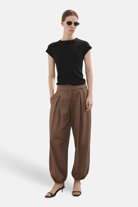 Top noir uni à manches courtes de MANGO, porté avec un pantalon plissé marron et des sandales foncées.