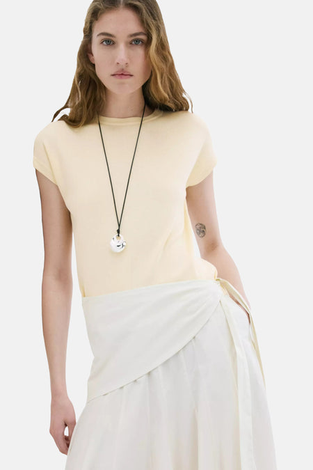 Top jaune à manches courtes de MANGO, texture côtelée, porté avec une jupe portefeuille blanche.
