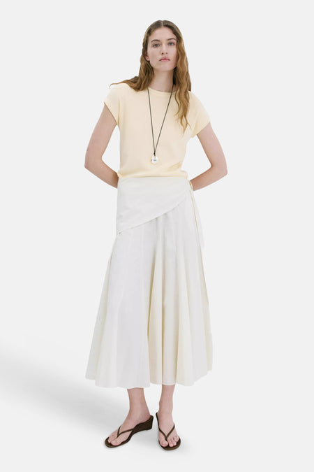 Top uni jaune à manches courtes de MANGO, porté avec une jupe blanche et des sandales.
