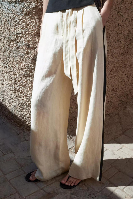 Lichtbeige broek van MANGO, met zwarte zijstrepen, wijde pasvorm en strikceintuur.
