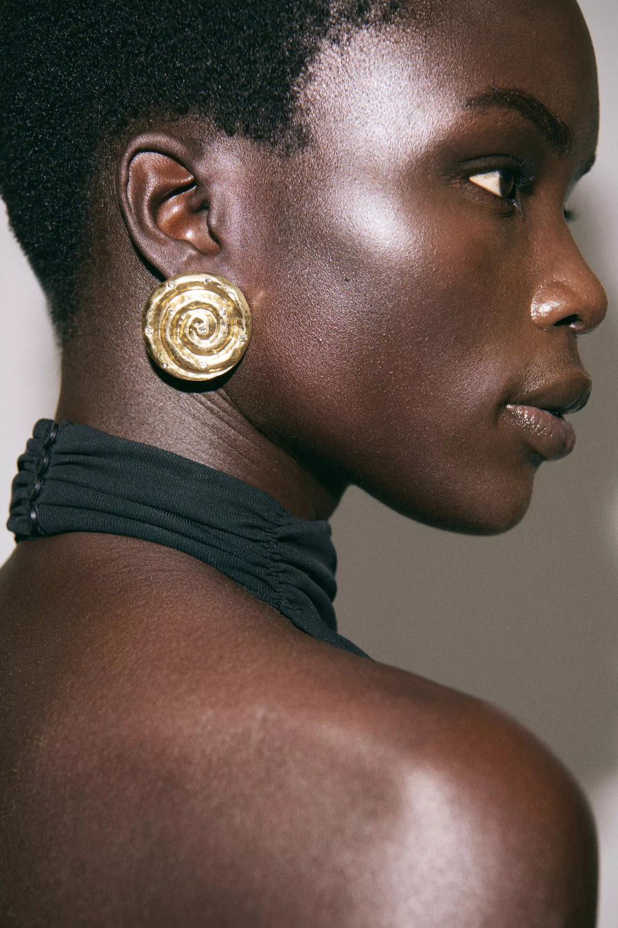 Gouden oorbellen van MANGO, met spiraalmotief en kleine ingelegde steentjes, op een model.