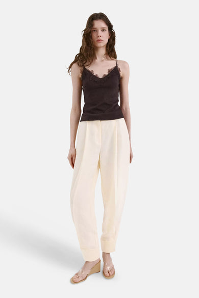 Brown lace-trimmed spaghetti strap top with delicate floral detailing, front view on model wearing cream trousers and clear wedge sandals.