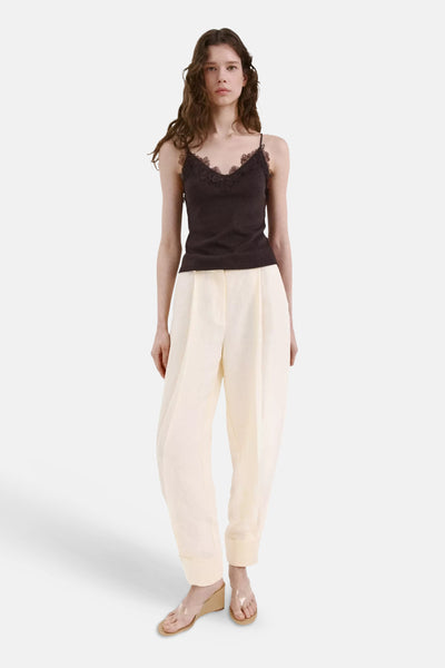 Brown lace-trimmed spaghetti strap top with delicate floral detailing, front view on model wearing cream trousers and clear wedge sandals.