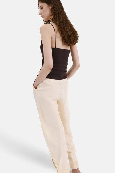 Brown ribbed knit tank top with thin straps, shown from side view on model wearing cream trousers.