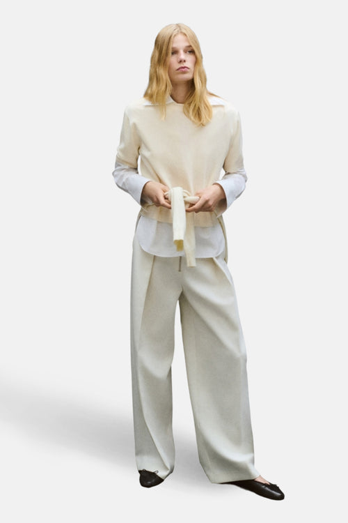 Pull à col rond écru de MANGO, porté avec une chemise blanche et un pantalon taille haute.