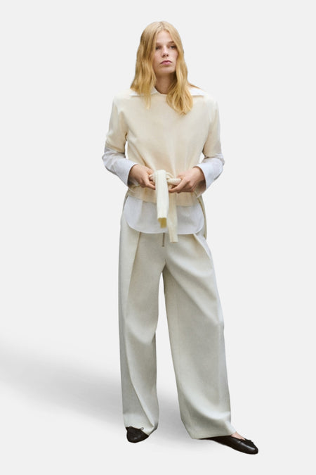 Pull à col rond écru de MANGO, porté avec une chemise blanche et un pantalon taille haute.