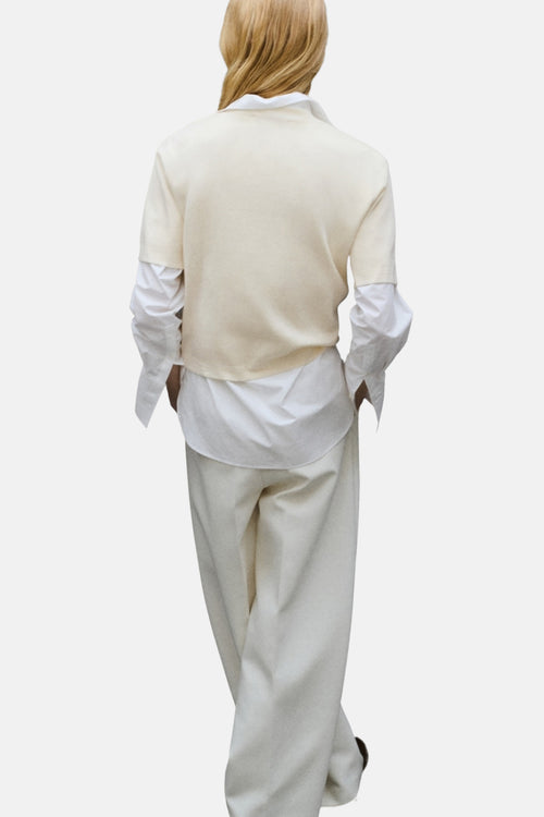 Pull à col rond écru de MANGO, porté sur une chemise blanche à manches longues et un pantalon blanc ample.