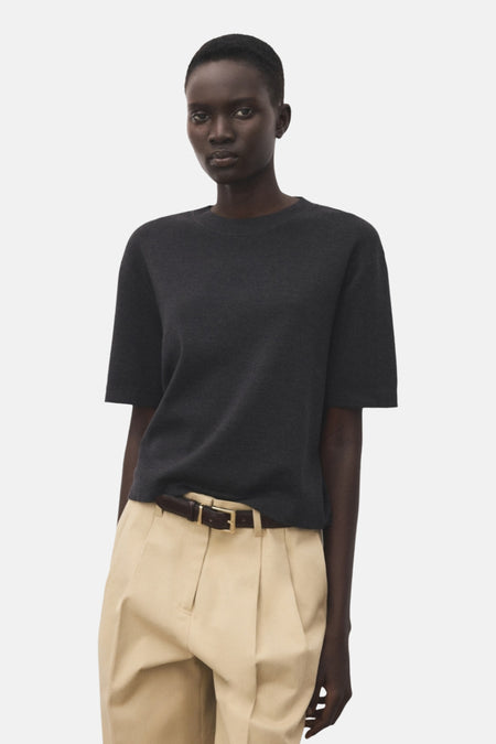 Pull à col rond gris de MANGO, porté avec un pantalon beige à ceinture marron.