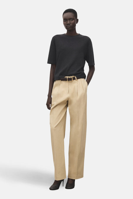 Pull à col rond gris de MANGO, porté avec un pantalon beige à plis et une ceinture en cuir marron.