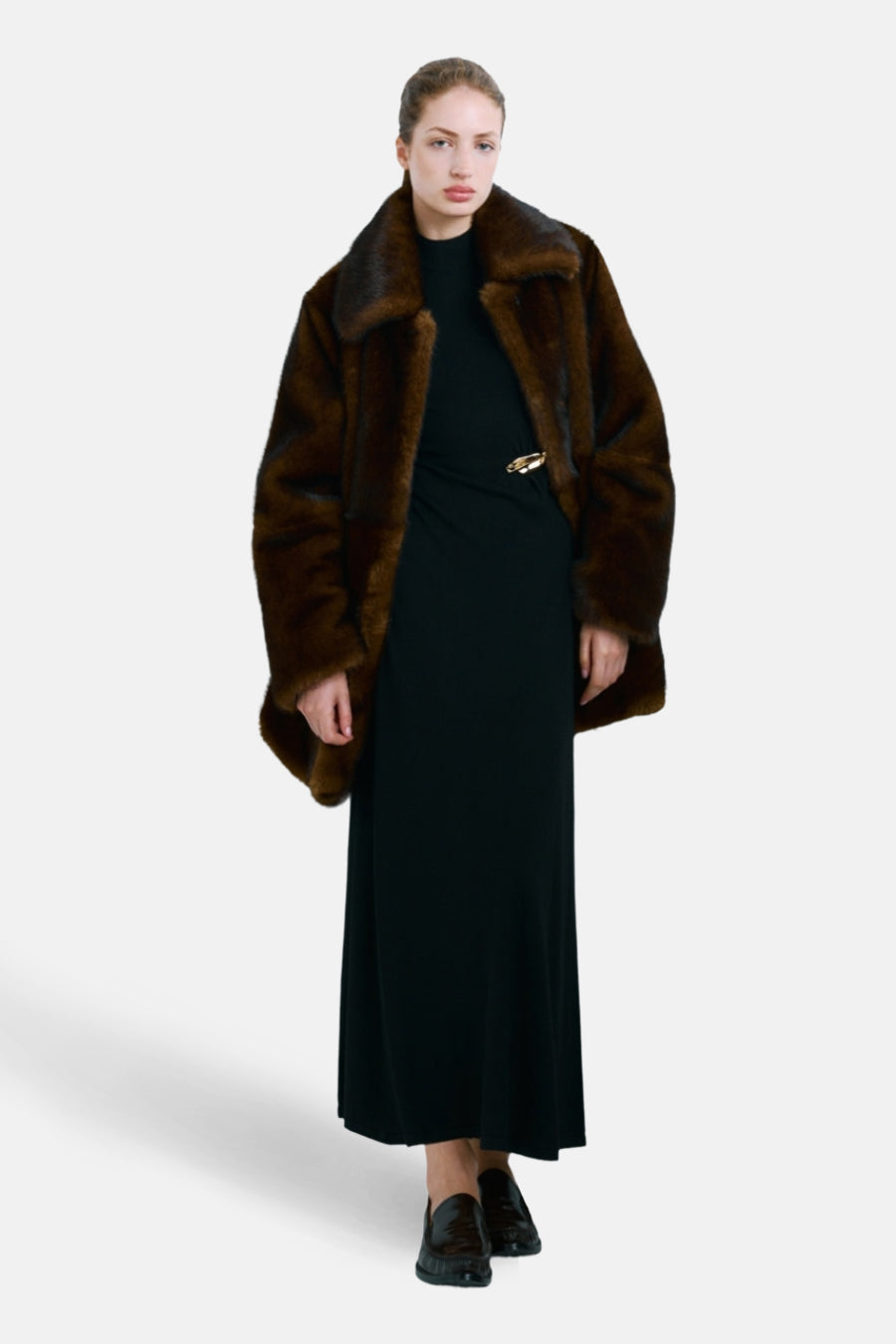 Zwarte jurk van MANGO, lang en vloeiend met een gouden speld en gedragen met een bruine bontjas.