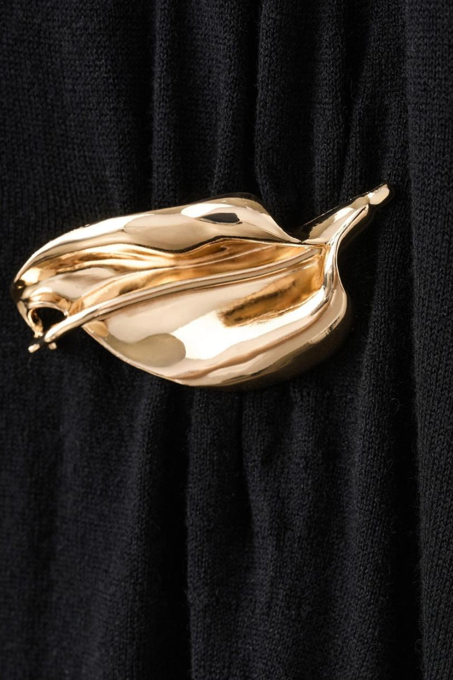 Zwarte jurk van MANGO met een gebreide textuur en een decoratieve gouden broche.