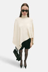 Ecru poncho van MANGO, gedragen over een zwarte jurk met panty en hoge hakken.