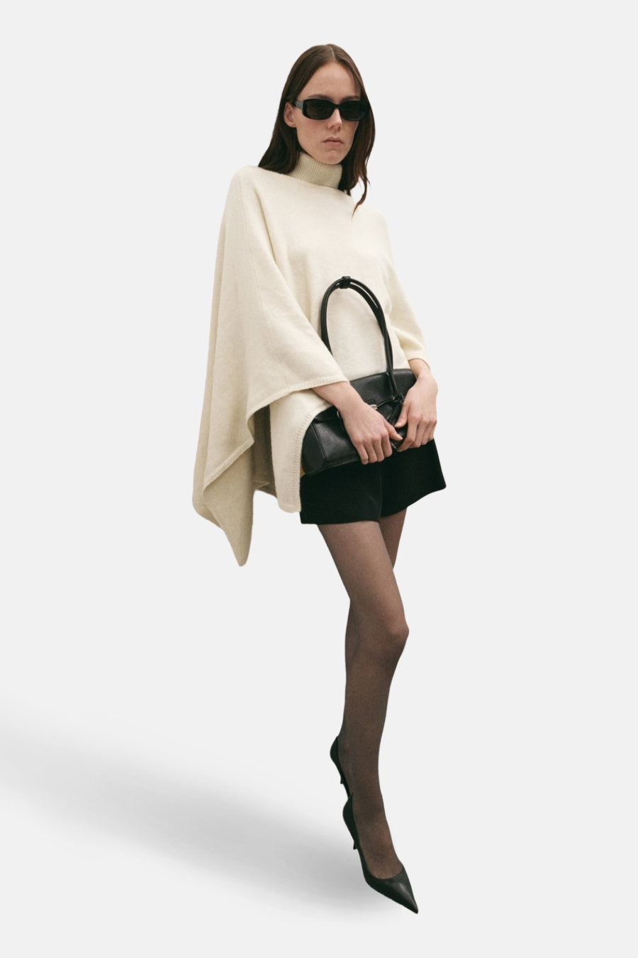 Ecru poncho van MANGO, gedragen met een zwarte panty, puntige pumps en een zwarte handtas.