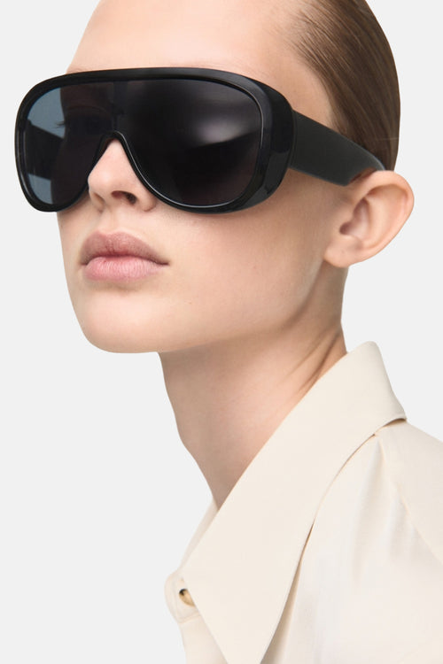 Chemise à manches longues écrue de MANGO, portée avec des lunettes de soleil noires sur un fond clair.