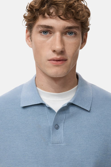 Blauwe V-hals trui van MANGO, gedragen over een wit T-shirt met ronde hals, op een effen achtergrond.