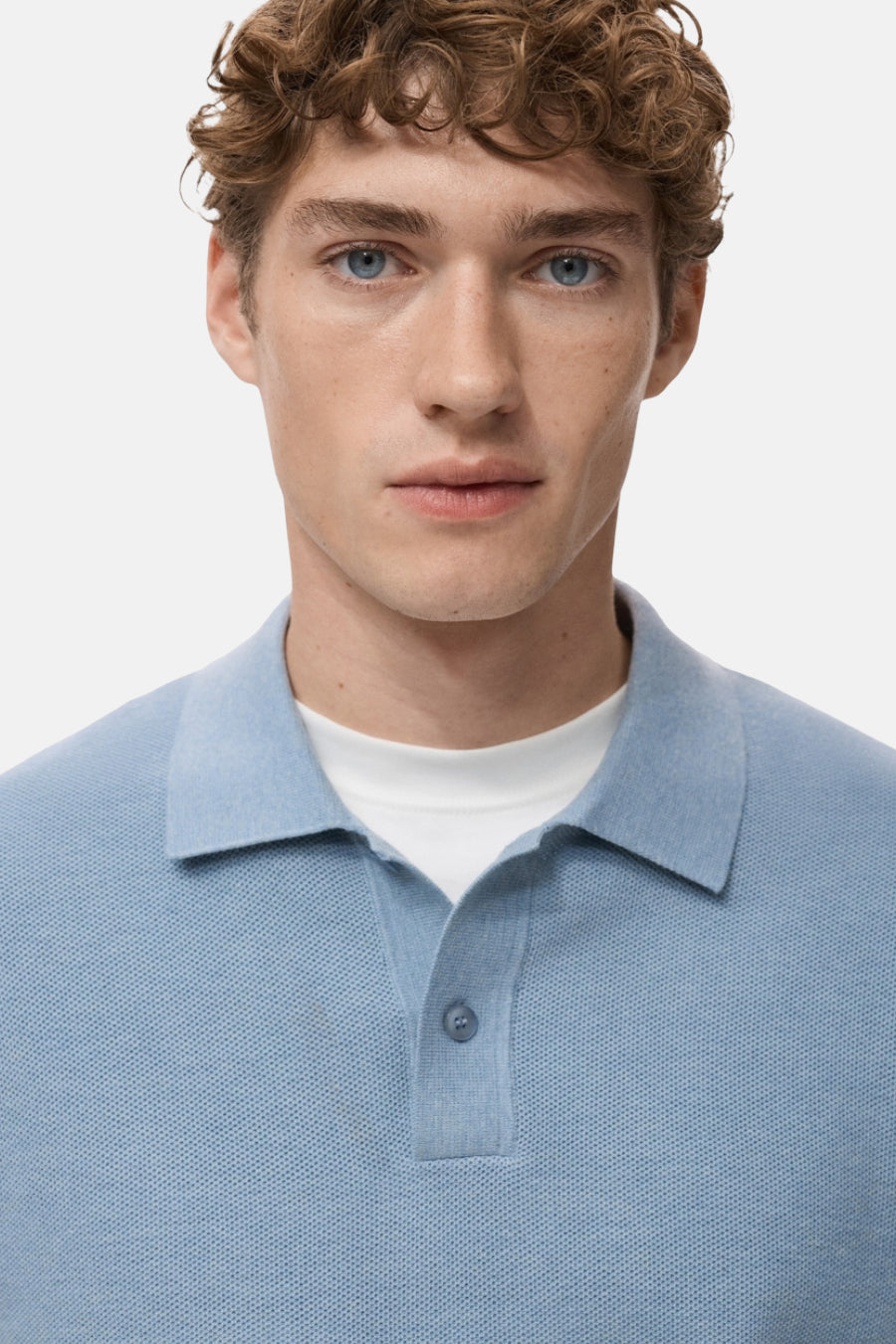 Blauwe V-hals trui van MANGO, gedragen over een wit T-shirt met ronde hals, op een effen achtergrond.