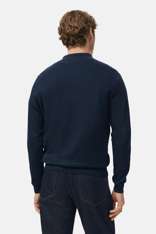 Pull à col en V bleu de MANGO, porté avec un jean bleu marine, vue de dos.
